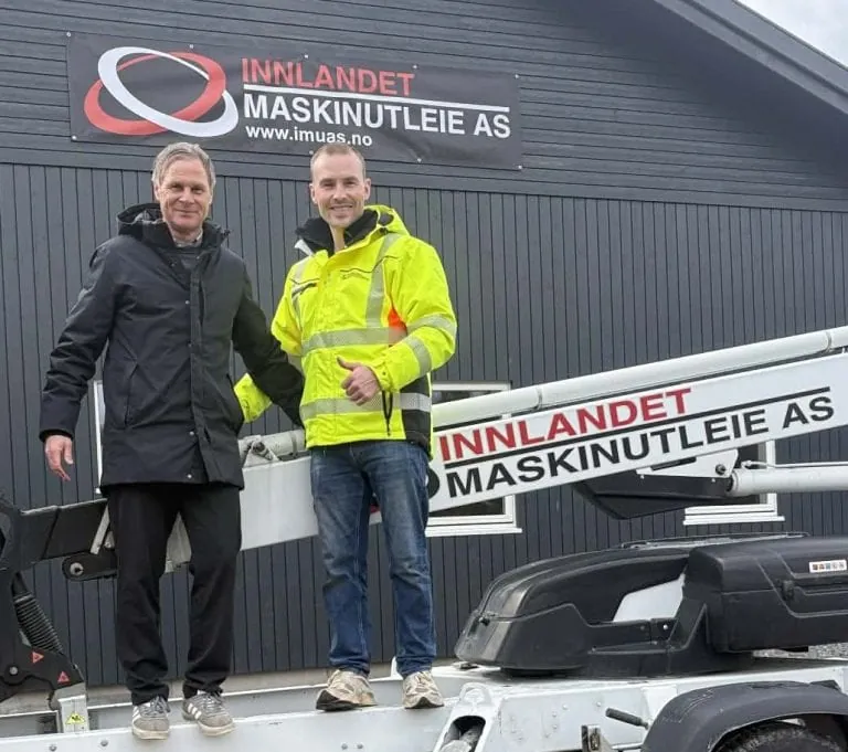 To ansatte foran Innlandet Maskinutleie sitt hovedkontor på Dokka med firmabil