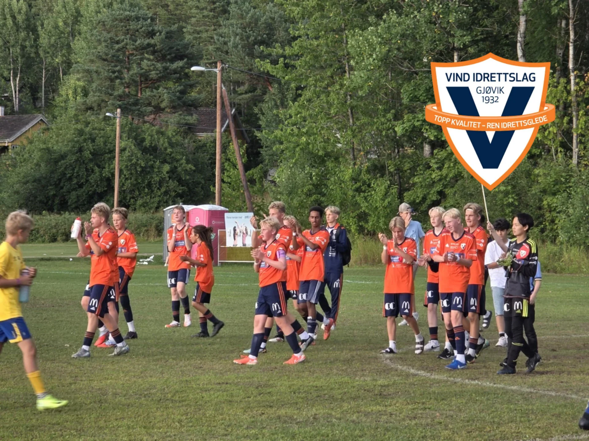Vind IL fotballspillere og trenere samlet på fotballbane med klubblogo synlig i bakgrunnen